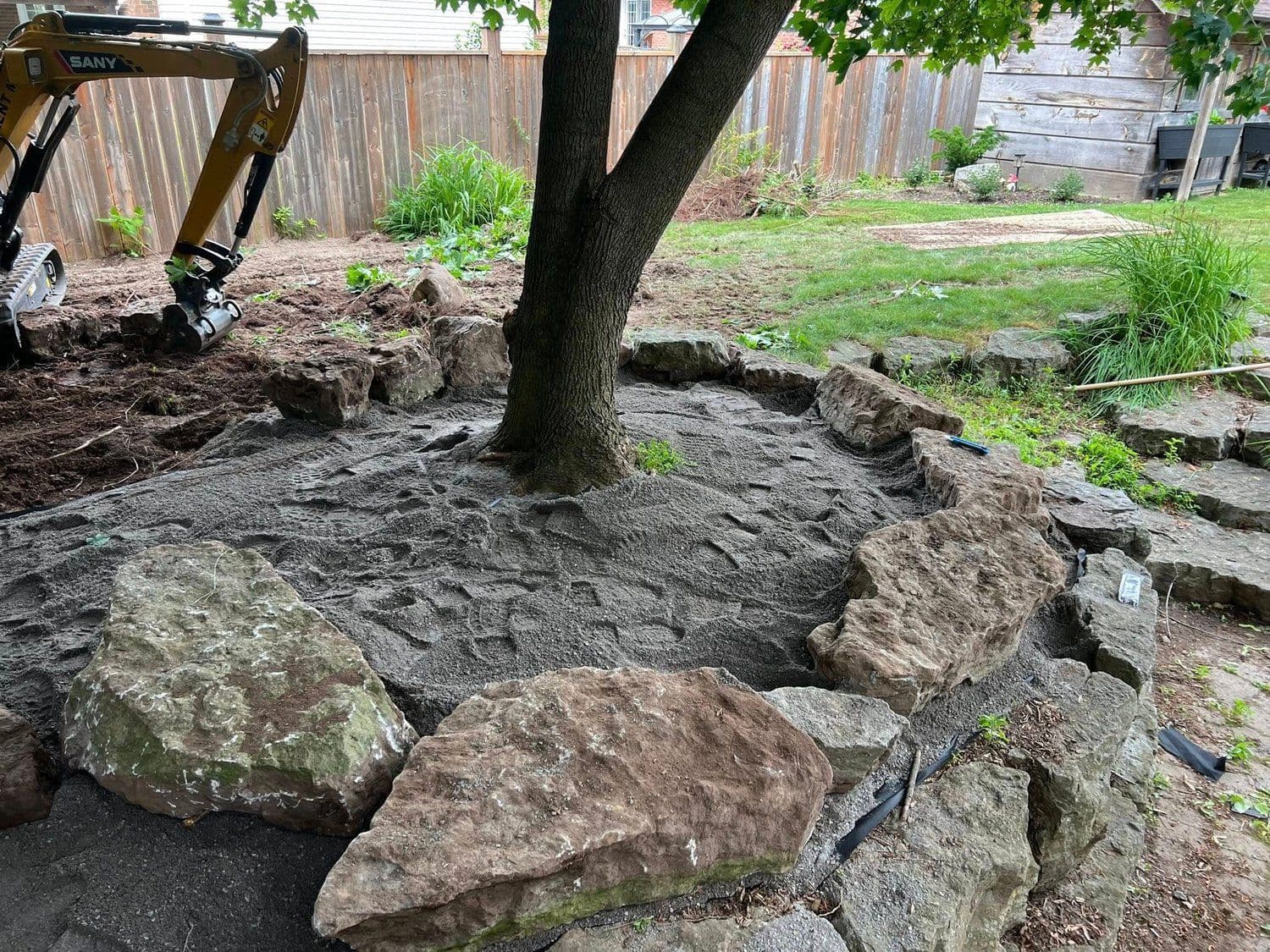 Compact excavator placing armor stone around a backyard tree
