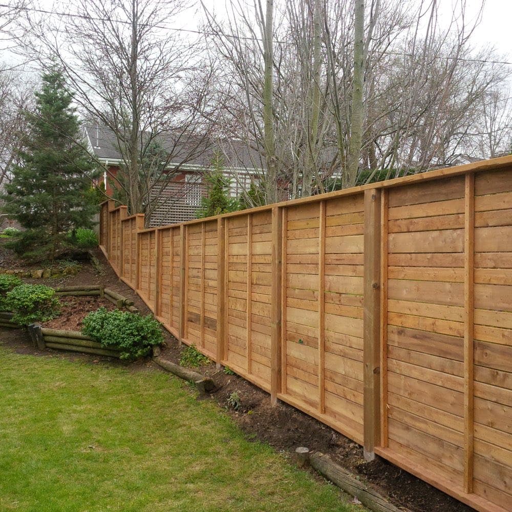 Tall horizontal-slat cedar privacy fence along a backyard line